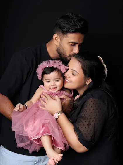 A classic family portrait against a simple black background, making the love and connection the true focus. The parents' gentle embrace and the baby's sweet smile make this a timeless keepsake.