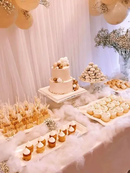 A dreamy, all-white dessert table that feels as light as a cloud. This setup features a two-tiered cake, cupcakes, and other sweets nestled in soft, fluffy textures and accented with delicate baby's breath, creating a heavenly display for your celebration.