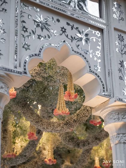 A close-up of the mandap decor, highlighting the delicate hanging florals and the beautiful mirror-work inlay on the traditional arches, blending artistry with elegance.