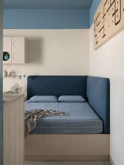 This son's bedroom in the 'Soft Serve' project uses soft blue tones and light wood to create a calm and playful atmosphere. The custom desk and overhead storage unit feature circular cutouts, adding a touch of modern geometry.