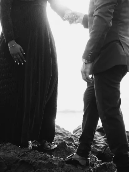 A minimalist black and white detail shot. The focus on their linked hands against the bright sky tells a simple but powerful story of connection and partnership.