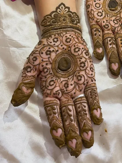 A close-up of a traditional mandala design on the palm, with cute heart details on the fingers.