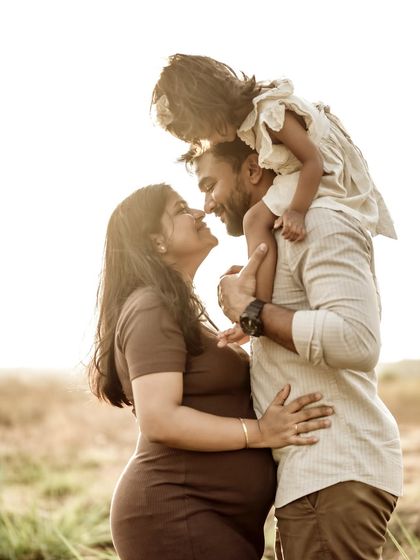 A loving family portrait in the golden sun. The daughter sits on her dad's shoulders, looking down at her mom, a beautiful image of their close-knit bond.