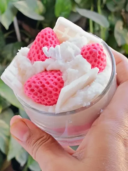 A close-up, hand-held view of the strawberry ice cream candle against a leafy background.