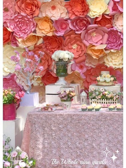 A "Bloom" themed first birthday dessert table set against a beautiful wall of handmade paper flowers in shades of pink and orange.