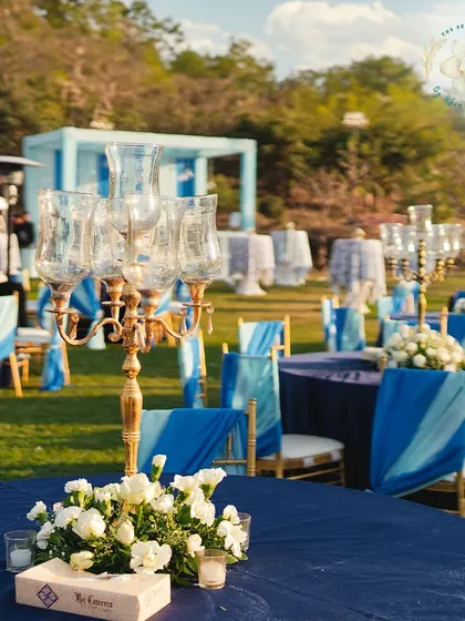 A Mehendi-Sangeet sundowner, where deep blues and crisp whites create an elegant and regal atmosphere. The gold candelabras and white floral centerpieces add a touch of classic luxury.