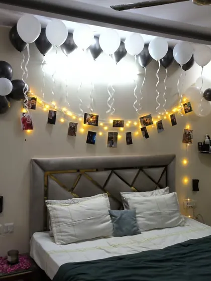 A cozy birthday bedroom setup featuring black and white balloons, with fairy lights and photos clipped along the string for a warm, personalized gallery wall.