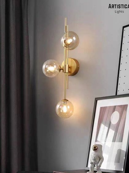 This vertical three-globe sconce adds a touch of modern glamour next to a bedside or in a hallway. The combination of clear glass globes and a linear brass structure creates a dynamic and stylish lighting fixture.