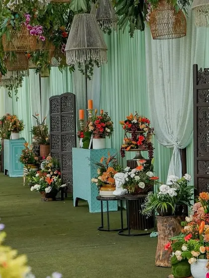 An elegant entrance pathway lined with antique screens and floral clusters on pedestals, all under a ceiling of hanging rattan chandeliers.
