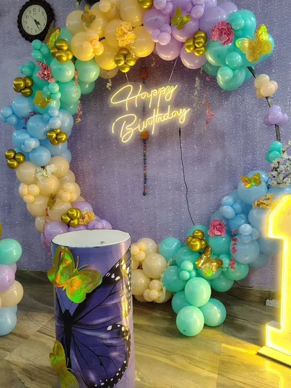 A full ring balloon arch in pastel colors for a butterfly-themed first birthday, complete with a neon sign and light-up number.