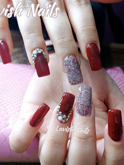 A rich, dark red set of square nails with accent nails in multi-colored glitter and pearl embellishments at the cuticle.