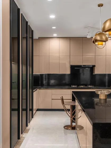This modern kitchen combines functionality with high-end aesthetics, featuring glossy beige cabinetry, a black granite island, and striking brass pendant lights. The layout is designed for effortless flow and entertaining.