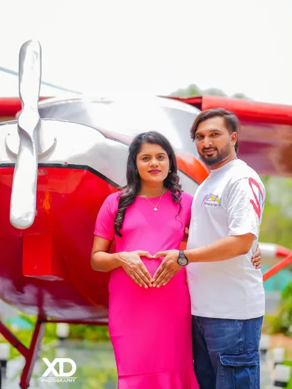 A happy couple's portrait in front of a vintage airplane, with their hands forming a heart on the baby bump.