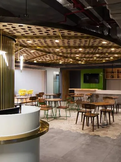 The cafeteria at the Carlsberg office, where a cylindrical, brass-finned column creates a striking focal point. The design uses industrial materials and brand-inspired details to craft a unique social hub.