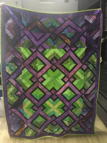 A complex geometric quilt in shades of purple and green, creating a mesmerizing, kaleidoscopic effect.