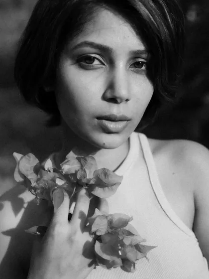 A close-up black and white portrait where the model is holding flowers. The soft natural light and monochrome treatment create a timeless and gentle mood.