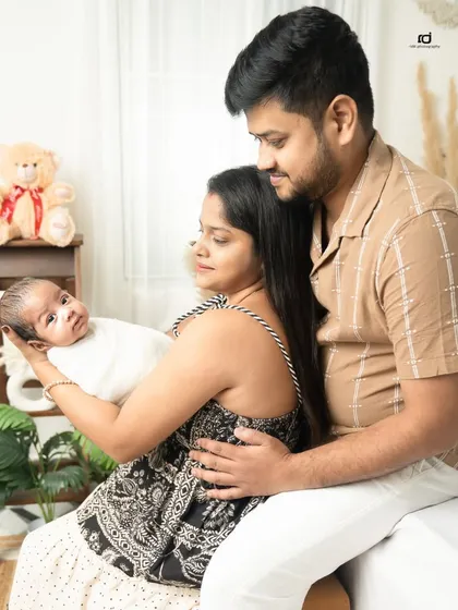 A quiet moment in the studio. The new parents admire their baby, who is looking right at the camera, creating a sweet and engaging family portrait.