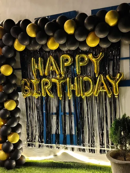 A simple yet bold birthday photo corner with a black and gold balloon frame against a black fringe curtain.