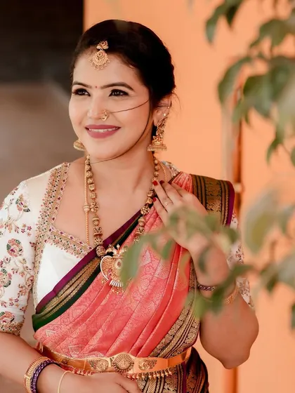 A bride wearing a white blouse with colorful floral embroidery on the sleeves. The blouse is paired with a pink and green silk saree, creating a fresh and vibrant look.