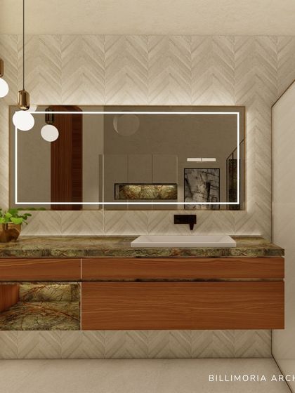 This bathroom vanity combines a wooden base with a green marble countertop and a backlit mirror. The herringbone pattern of the wall tiles adds a subtle texture, creating a space that is both modern and warm.