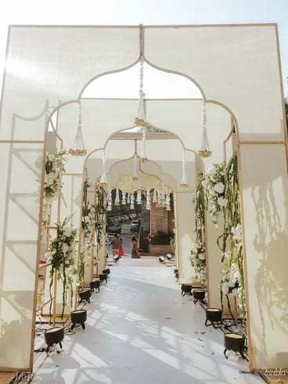 A grand arched entranceway for Aashvi and Akash's wedding, decorated with delicate white floral arrangements and hanging tassels. This created a soft and timeless passage into the main ceremony area.