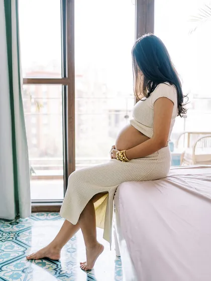 A pensive moment as the mother-to-be sits on the edge of the bed, looking out the window. It captures the quiet contemplation and anticipation that is such a big part of pregnancy.
