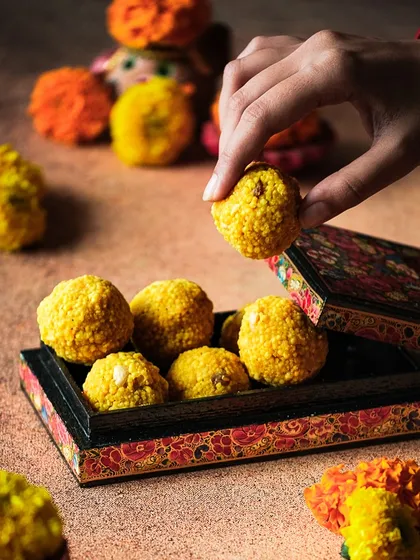 A close-up action shot of a hand picking up a laddoo. This type of shot is engaging and makes the viewer want to reach in and grab one too.