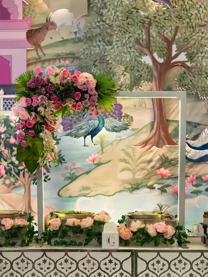 A stunning buffet station set against a hand-painted backdrop of a pastoral scene. The floral arrangements are designed to complement the artwork, creating a cohesive and artistic theme.