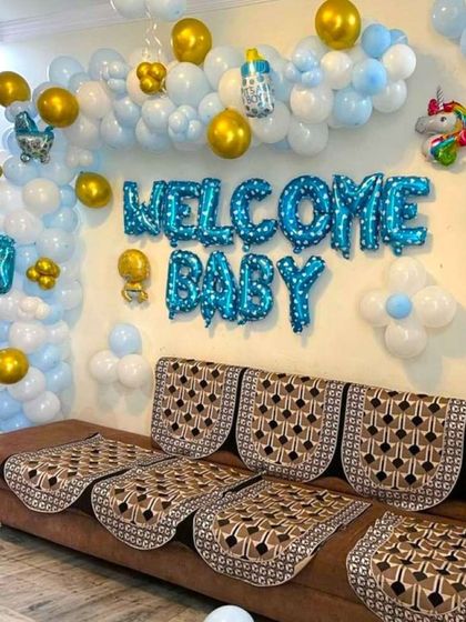A 'Welcome Baby' decoration for a baby boy's arrival at home. The living room is decorated with blue, white, and gold balloons and foil letters.
