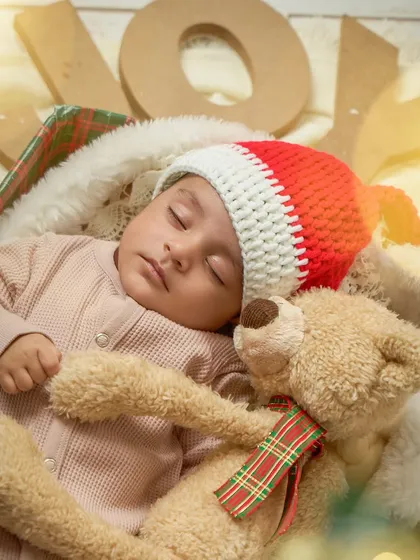 A newborn sleeps peacefully with a teddy bear during a Christmas mini session. The Santa hat and festive details make this an incredibly sweet 'baby's first Christmas' portrait.