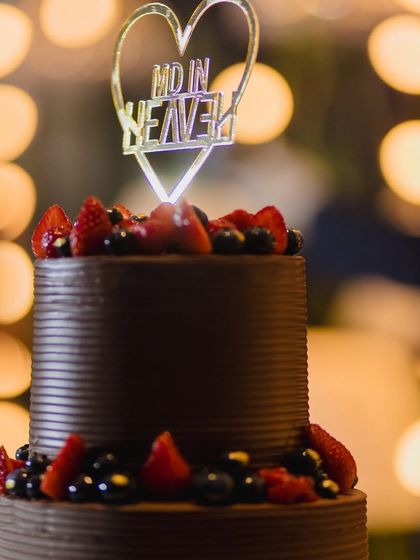 A close-up of the custom "Made in Heaven" topper on the berry-covered chocolate wedding cake, with beautiful bokeh lights in the background. It’s the little details that make a celebration truly personal.