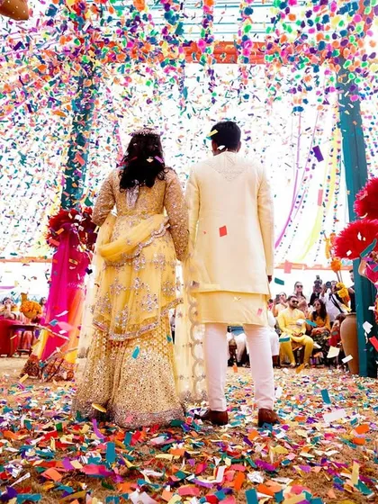 A beautiful shot from behind the couple as they enter through a shower of colorful confetti, surrounded by dancers.