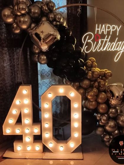 A stylish setup for a 40th birthday with a black and gold balloon half-arch and large marquee numbers.