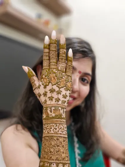 A playful pose showing off one full arm of traditional mehendi, with lotus patterns on the fingers and classic bands on the arm.