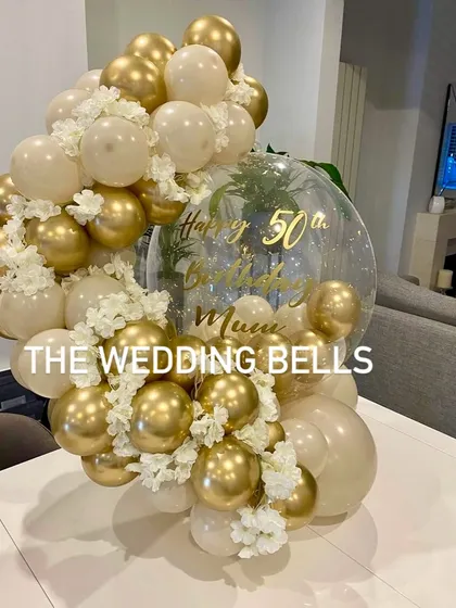 A beautiful and elegant balloon centerpiece designed for a mother's 50th birthday. The combination of chrome gold and soft white balloons, accented with delicate white flowers, creates a sophisticated and celebratory look.