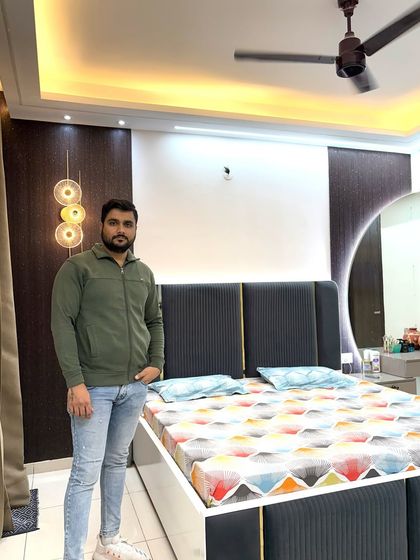 A master bedroom featuring a dark wood-paneled wall behind the bed, a round backlit mirror, and an upholstered headboard.