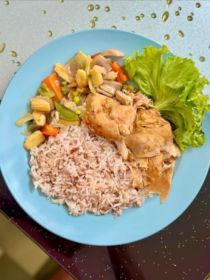 A healthy plate of red rice with steamed chicken and a side of Thai-style mixed vegetables.