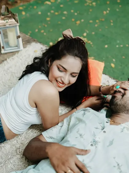 A cute and candid shot of the bride-to-be playfully covering her partner's eyes during their pre-wedding picnic.