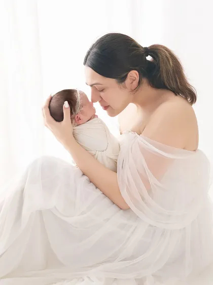 An intimate mother and child portrait, focusing on the gentle connection as she touches her nose to her baby's. The all-white styling creates a soft, ethereal feel, perfect for newborn photography.