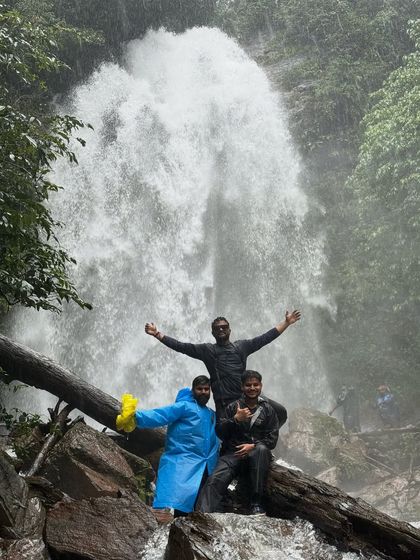 Three friends celebrating in front of Hidlumane Falls, their colorful raincoats bright against the powerful cascade.