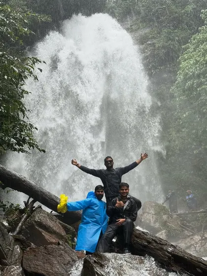 Three friends celebrating in front of Hidlumane Falls, their colorful raincoats bright against the powerful cascade.