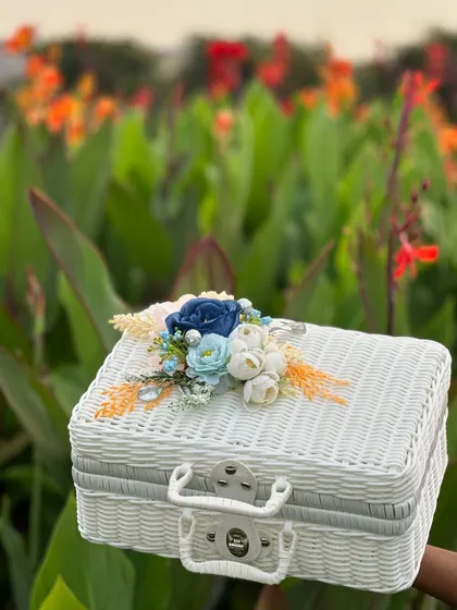 A white rattan style suitcase decorated with a cool blue floral arrangement. This shows how we can customize our baskets and boxes to suit any color theme or occasion.