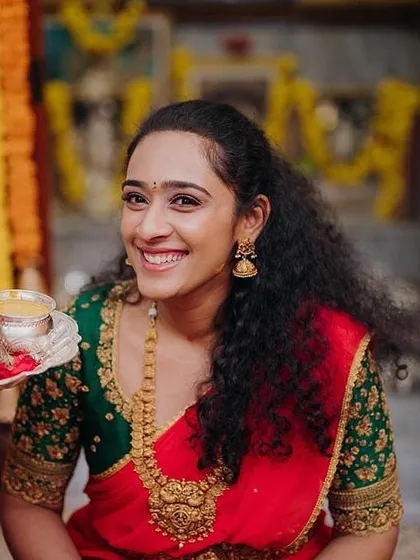 A bride's joyful moment during a pre-wedding ceremony. She wears a vibrant red saree with a contrasting green blouse featuring all-over floral embroidery.