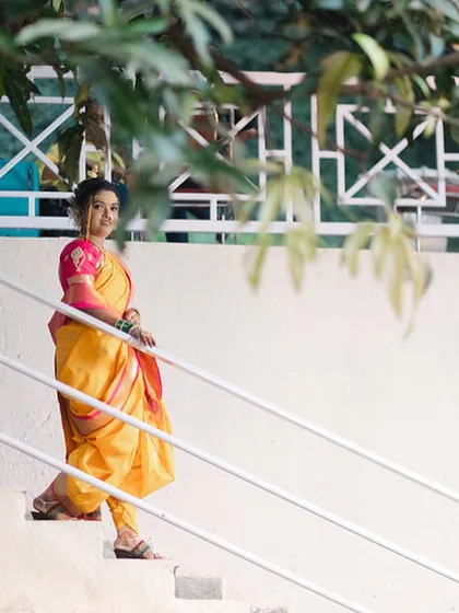 A full-length portrait of the bride in her yellow Nauvari saree, posing gracefully on a staircase.