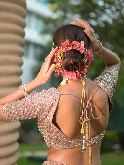 A back view of a romantic low bun adorned with a garland of vibrant pink orchids. This style is perfect for a destination wedding shoot or a spring fashion story.