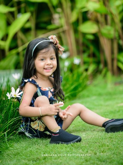 This little girl flashes a peace sign while sitting in the grass. It's a fun, candid shot that shows off her playful personality during her outdoor kids photoshoot.