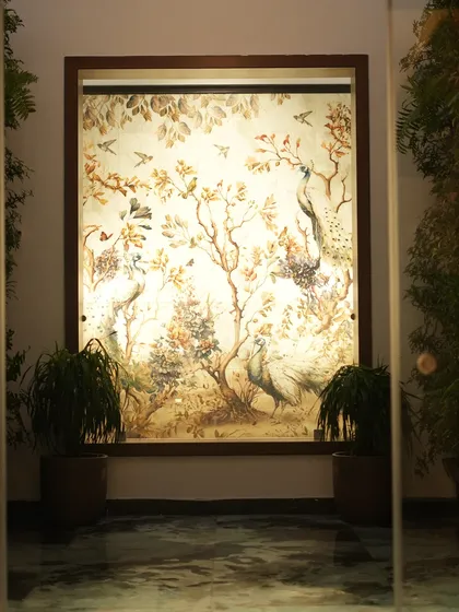 A wider shot of the illuminated peacock mural, showing how it acts as a stunning centerpiece in a hallway, enhanced by our plant styling.