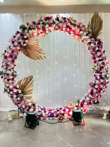 This circular floral mandap is a modern and artistic choice for a wedding ceremony. The ring, decorated with pink and purple flowers and accented with gold leaves, symbolizes eternity.