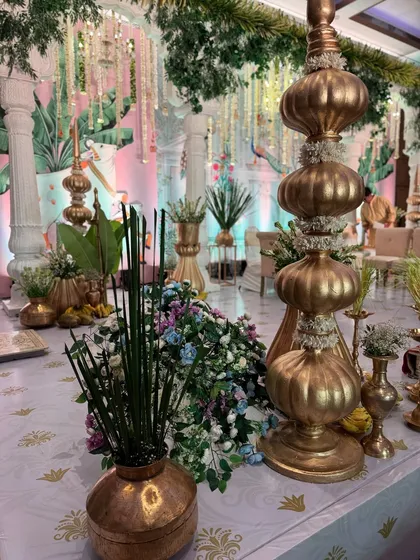A detailed shot of a table setting at a Pichwai-themed wedding, featuring golden decor pieces, traditional banana offerings, and a backdrop of artistic paintings.