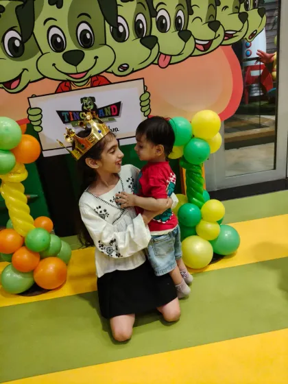 A sweet moment between siblings at a birthday celebration, complete with a birthday crown and colorful balloons.